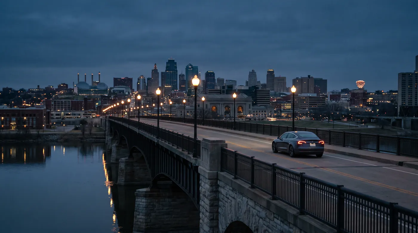 A dark sedan on a bridge over the river at night, the city lit behind it.